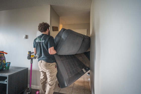 A crew member carrying a sofa out of an apartment