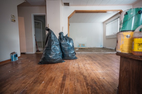 An emptied room with bare hardwood floors and the last bags of junk ready to go