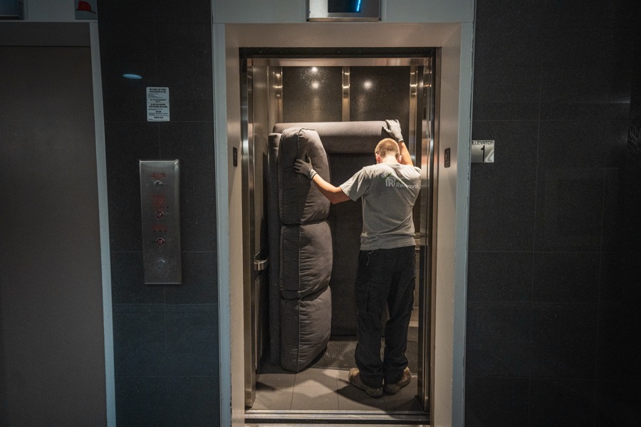 A crew member loading a rolled mattress into a commercial building elevator