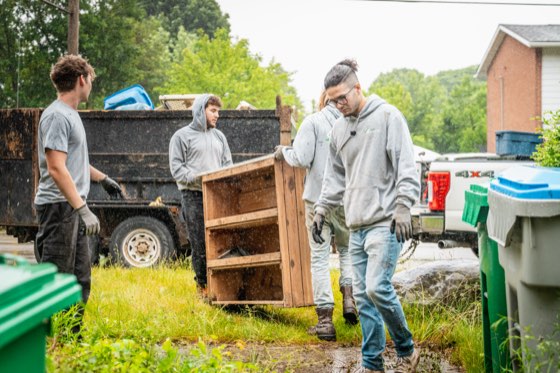 Three Complete Junk Removal crew members lifting an old wooden cabinet into the trailer behind their pickup truck