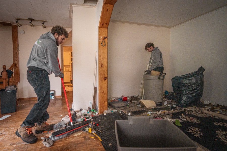 Two crew members shovelling and sweeping construction debris out of a gutted room