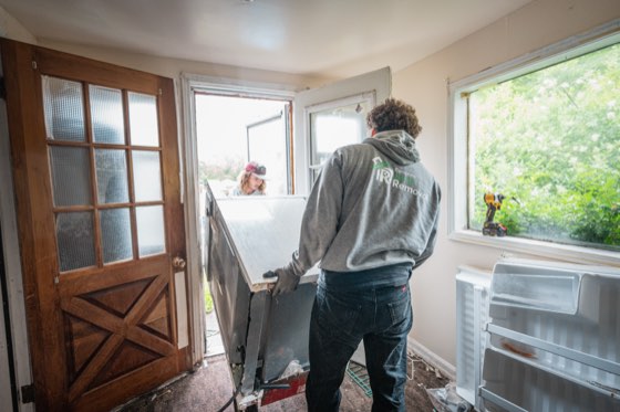 A crew member manoeuvring an old refrigerator out through a doorway