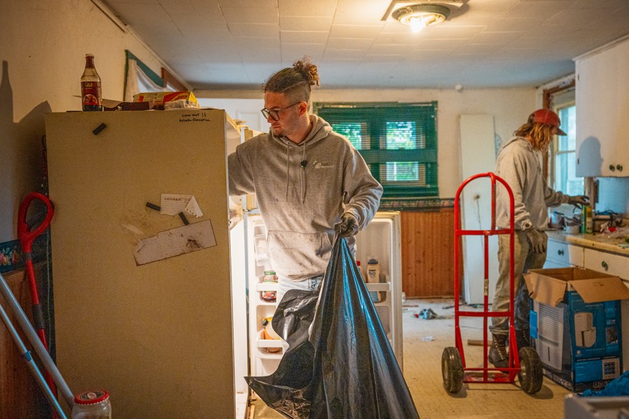 A crew member bagging household junk beside an old fridge during a kitchen cleanout
