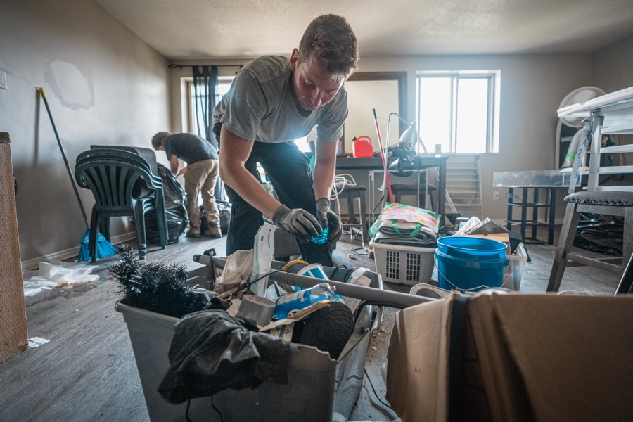 A gloved crew member sorting contaminated household junk into a bin