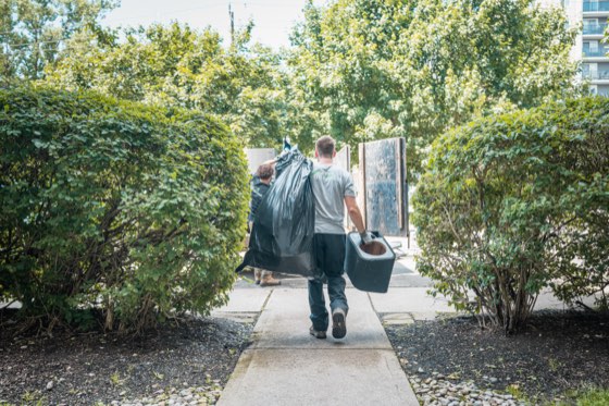 Two crew members carrying bagged yard waste and a bin down a garden path between trimmed hedges